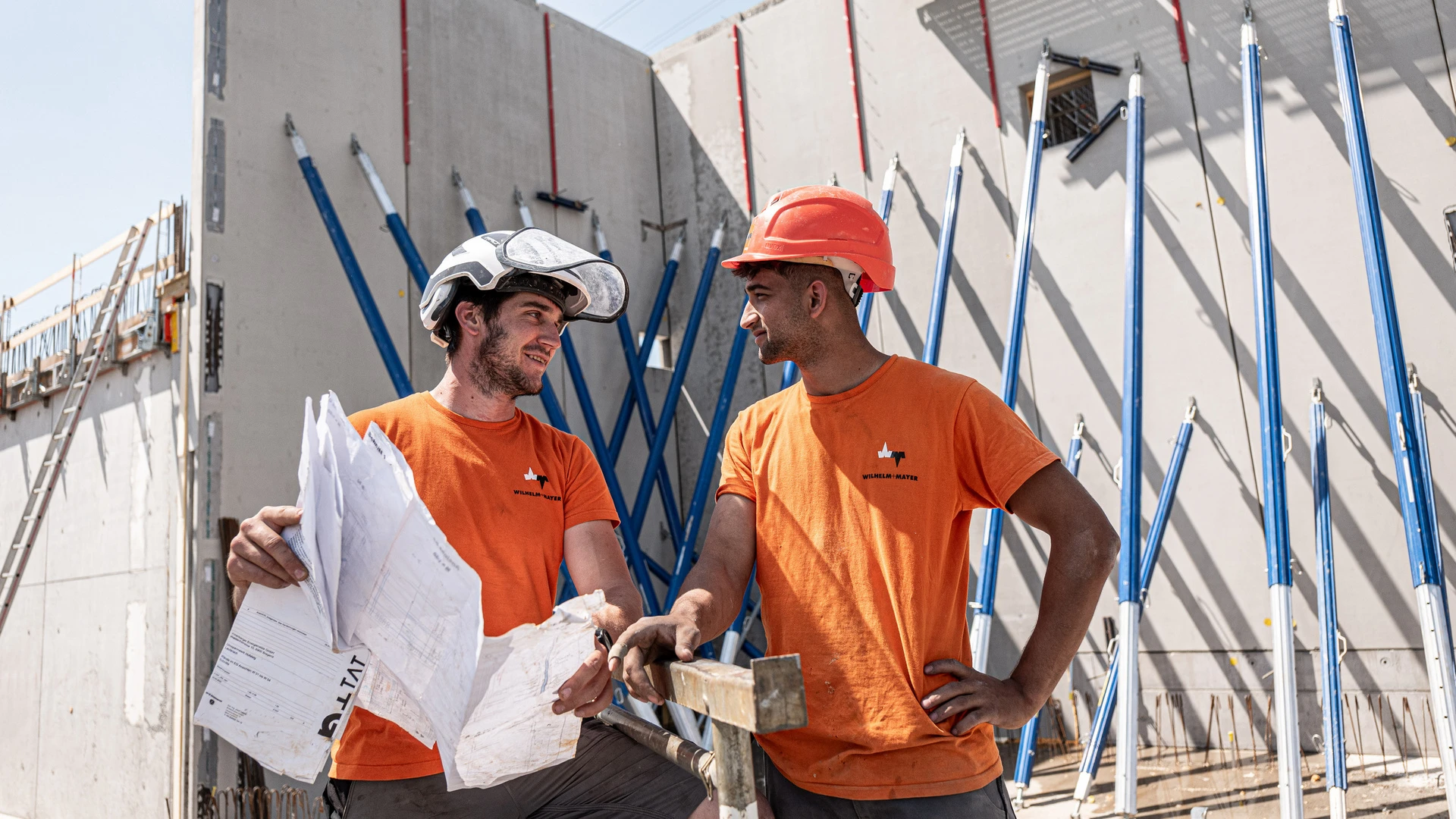 Zwei Bauarbeiter lesen einen Bauplan und lachen