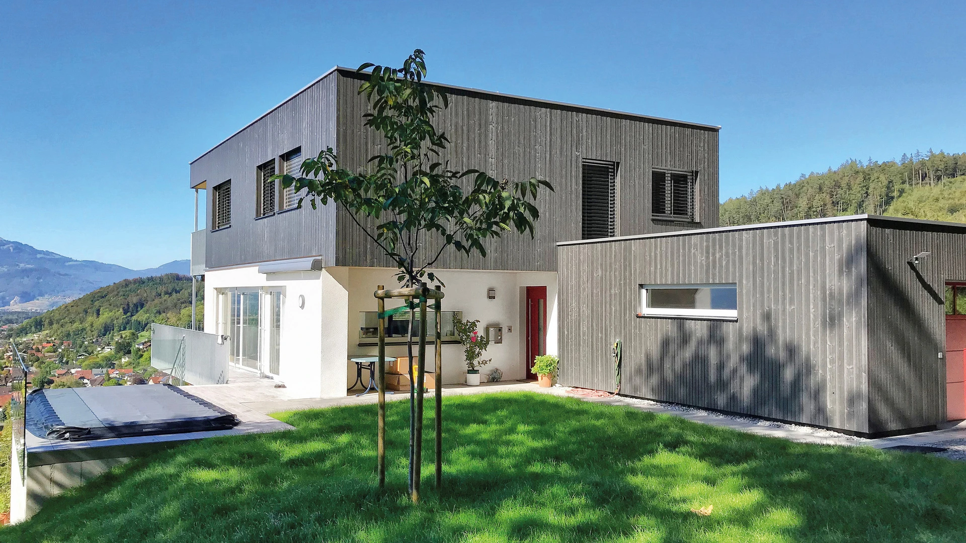 Fertiggestelltes Haus mit Flachdach in Hanglage nach Umbau und Sanierung. Abtragen bestehendes Satteldach, Sanierung und Aufstockung in Holzbauweise auf das bestehende Wohnhaus. Errichtung einer Garage im nordöstlichen Bereich.
