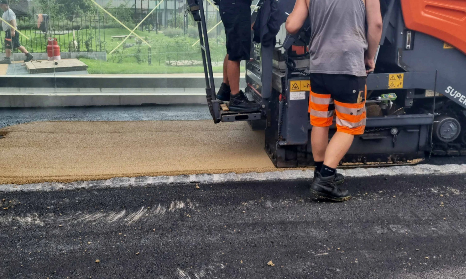 Fertiger und Arbeiter vor Bushaltestelle bei Asphaltierarbeiten von Wilhelm+Mayer Bau am Garnmart in Götzis.