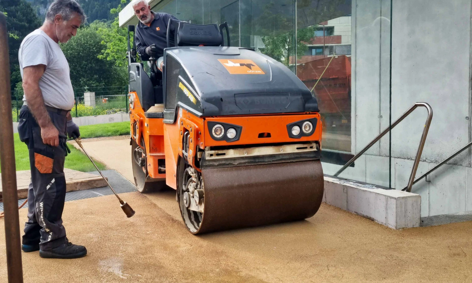 Walze und Arbeiter vor Bushaltestelle bei Asphaltierarbeiten von Wilhelm+Mayer Bau am Garnmart in Götzis.