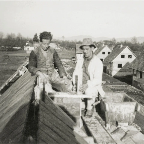 Erwin Mayer und ein Mitarbeiter bauen den Kaminabschluss eines Siedlungshauses