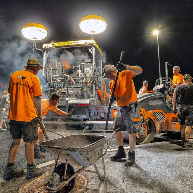 Eine Asphaltbau-Partie von Wilhelm-Mayer arbeitet in der Nacht. Große Maschinen und Walzen bringen den neuen Straßenbelag auf.