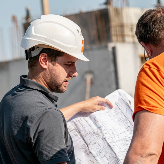 Auf einer Wilhelm-Mayer Baustelle wird fleißig gearbeitet. Bauleiter und Mitarbeiter blicken auf einen Plan und besprechen die nächsten Arbeiten.