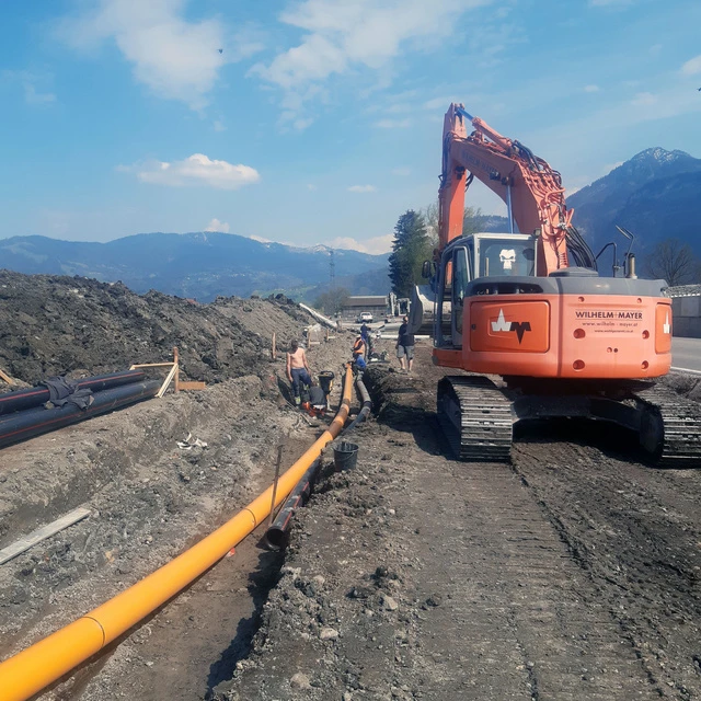Eine Partie von Wilhelm-Mayer Tiefbau verlegen Leitungen. Daneben steht ein Bagger.