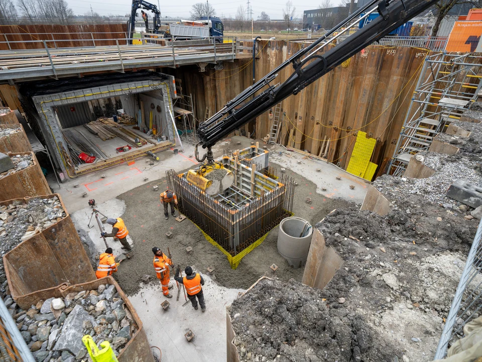 Arbeiter stehen in einer großen Baugrube mit Spundwänden links und rechts. Hier wird eine Bahnunterführung errichtet.